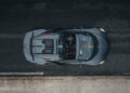 Overhead view of a sleek, dark-colored convertible sports car on a road, displaying the detailed interior and exterior features of the Bugatti W16 Mistral with an open top, hinting at its potential to break speed records.