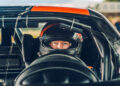 A race car driver, donning a helmet, is seated inside a sleek Bugatti W16 Mistral, viewed through the windshield.