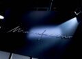 A silver script sign reading "Manufaktur" on a dark wall, illuminated by a spotlight from above, evokes the artistry of the Mercedes-Benz MANUFAKTUR Studio, where customization meets excellence.