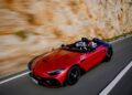 A red Mercedes-AMG sports car with a number 10 decal speeds along a road beside a rocky wall. The driver, clad in a helmet, embodies PureSpeed.