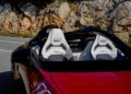 The Mercedes-AMG PureSpeed red convertible, with its sleek white seats, is parked on a road beside the rugged rocky terrain, revealing a perfect blend of style and power.