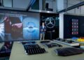 A man stands in MANUFAKTUR Studio, a modern showroom where Mercedes-Benz showcases its extensive customization options. Various automotive components are meticulously arranged on tables, inviting exploration and creative inspiration.
