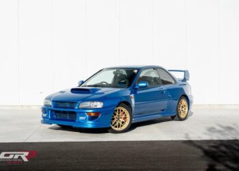 A rare 1998 Subaru Impreza WRX STi 22b with gold wheels is parked in front of a white wall. For sale to collectors and enthusiasts, this blue sports car captures the spirit of a thrilling legacy.