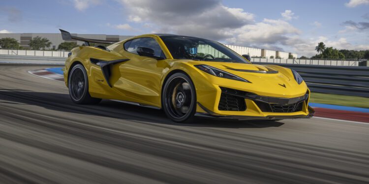 A yellow sports car speeding on a race track with motion blur and a cloudy sky in the background.
