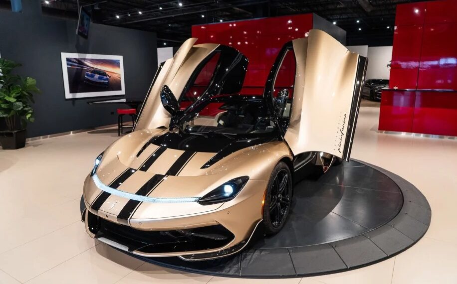 A gold and black electric hypercar with its scissor doors open is displayed in a showroom with a red and black backdrop, highlighting the stunning Pininfarina Battista for sale.