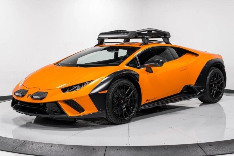 The Lamborghini Huracán Sterrato, an orange sports car with black accents and a roof rack, commands attention as it spins elegantly on a rotating platform in the showroom.