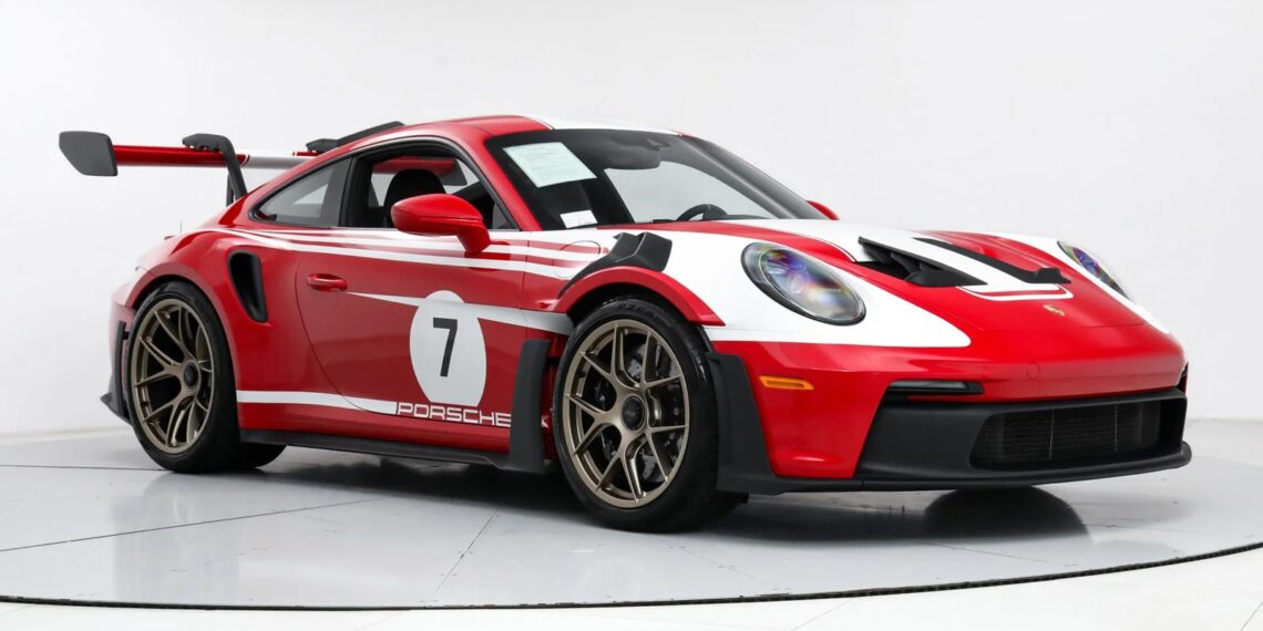 A red and white Porsche 911 GT3 RS with racing decals, including the iconic number 7, gleams under the lights in a pristine white room.