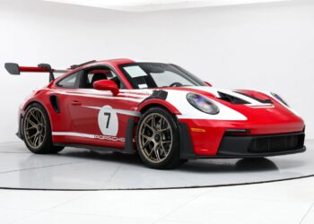 A red and white Porsche 911 GT3 RS with racing decals, including the iconic number 7, gleams under the lights in a pristine white room.