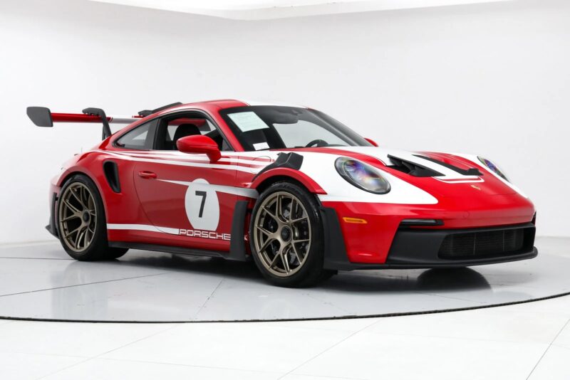 A red and white Porsche 911 GT3 RS with racing decals, including the iconic number 7, gleams under the lights in a pristine white room.