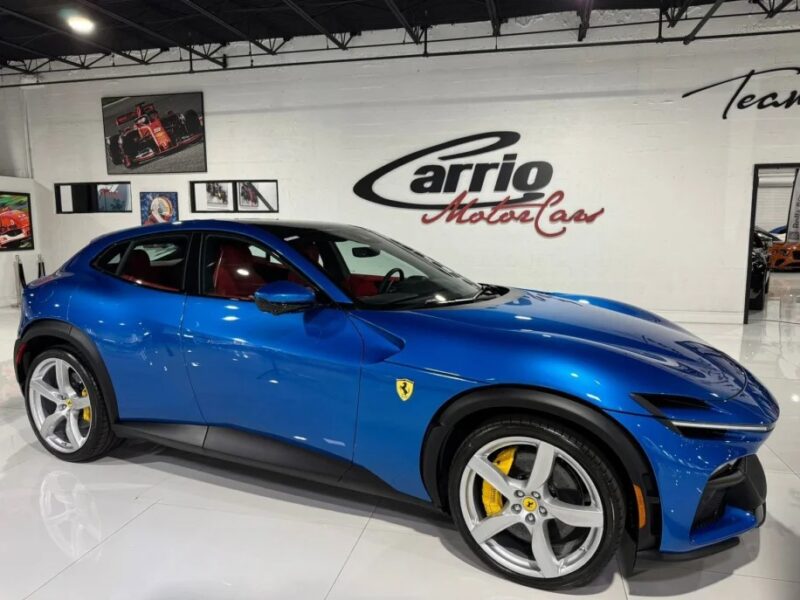 Mobil sport mewah biru dipamerkan di ruang pamer yang ramping dengan dinding putih, menampilkan branding Ferrari dan menggoda keanggunan SUV Purosangue.