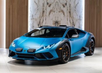 A blue Lamborghini Huracán Sterrato with a sleek design is parked indoors, featuring a marble wall and wooden paneling in the background.