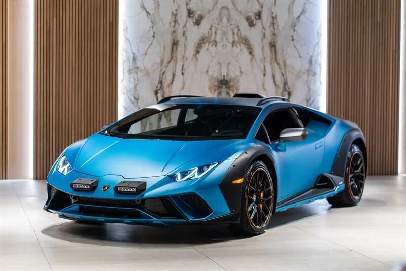 A blue Lamborghini Huracán Sterrato with a sleek design is parked indoors, featuring a marble wall and wooden paneling in the background.