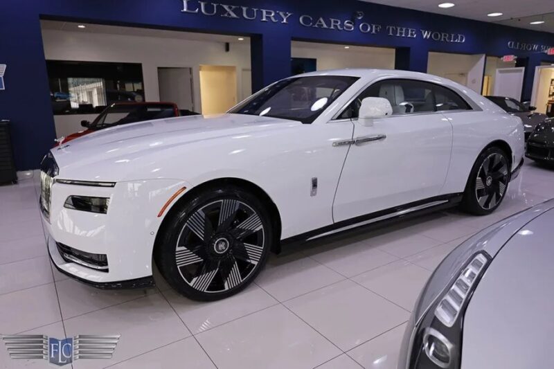 A Rolls-Royce Spectre, the epitome of electric ultra-luxe, graces the showroom floor. This super coupe boasts a sleek design with black rims, capturing attention with its elegant aura.