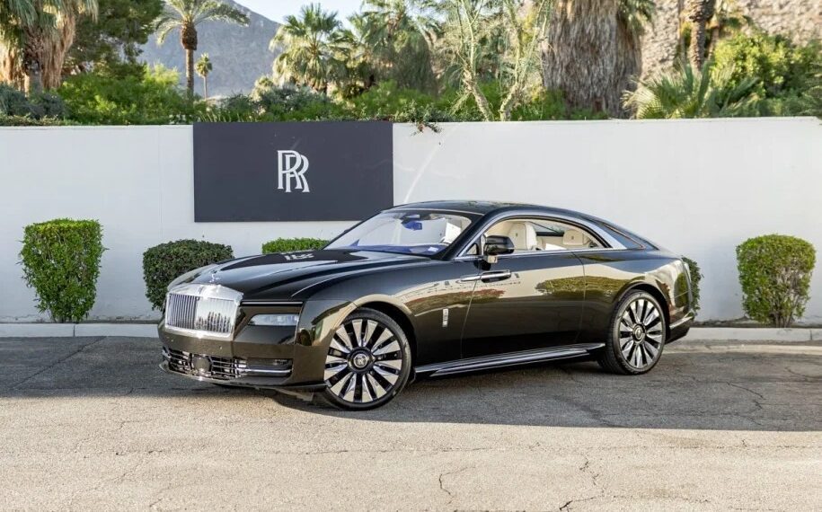 A sleek black ultra-luxe coupe is parked in front of a white wall with palm trees in the background, embodying the elegance and innovation of the Rolls-Royce Spectre.