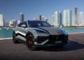 A luxury Lamborghini SUV, part of the prestigious Ad Personam Program, is parked by a waterfront with a city skyline in the background under a clear blue sky.