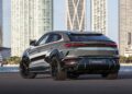 A sleek Lamborghini Urus SE with geometric patterns is parked on a waterfront, silhouetted against the vibrant skyline, capturing the essence of Art Basel 2024 in the background.