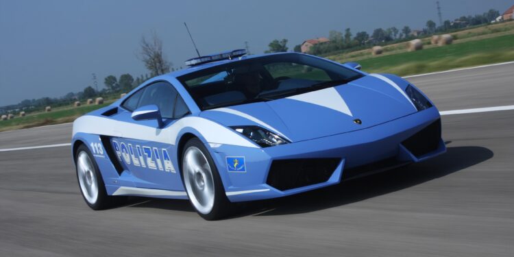 A blue and white Lamborghini of the Italian State Police zips down the road, against a blurred backdrop, highlighting their celebrated 20-year partnership with luxury speed.