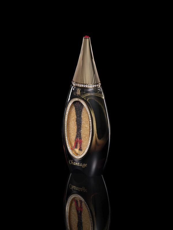 The 2024 Holiday Gift Guide features a black and gold perfume bottle with a teardrop shape and pointed cap, elegantly poised on a reflective surface, ideal for luxury enthusiasts.