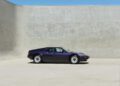 A purple BMW M1 sports car, with its sleek design, is parked in an empty, minimalist concrete space under a clear blue sky—a fitting scene for a collaboration with KITH designed by Ronnie Fieg.