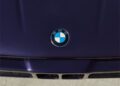 Close-up of a purple car hood featuring the iconic BMW logo, with echoes of the legendary BMW M1, centered above two air vents. This design element is reminiscent of the collaborative elegance often seen in partnerships like Ronnie Fieg's creations for KITH.