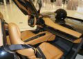 The interior of this luxury sports car, displayed at Braman Motorcars in Palm Beach, features elegant tan leather seats and a sleek black helmet resting on the passenger seat. Its open scissor doors invite admiration and hint at the Automobili Pininfarina craftsmanship within this upscale showroom.