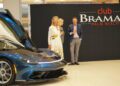 Three people stand beside a stunning blue sports car at the Braman Motorcars event in Palm Beach, celebrating automotive excellence synonymous with Automobili Pininfarina.