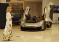 A woman in a floral skirt observes an Automobili Pininfarina with butterfly doors open in a well-lit Braman Motorcars showroom.