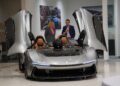 In the showroom of Braman Motorcars in Palm Beach, a sleek silver sports car with winged doors open exudes elegance. Two people stand behind it, admiring the exquisite craftsmanship of Automobili Pininfarina.