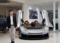 A person in a suit strolls through the Braman Motorcars showroom in Palm Beach, passing by a sleek silver sports car with open butterfly doors, reminiscent of Automobili Pininfarina's elegant designs.