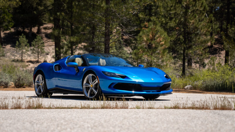 A blue sports car parked on a paved area surrounded by trees and greenery.