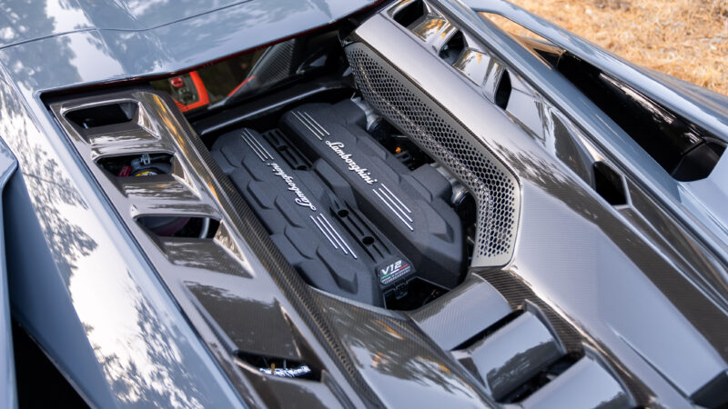 View of a Lamborghini V12 engine in a car's engine compartment, surrounded by carbon fiber components.