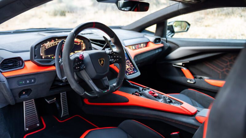 Interior of a sports car featuring a sleek steering wheel, digital dashboard, and red-accented black seats.