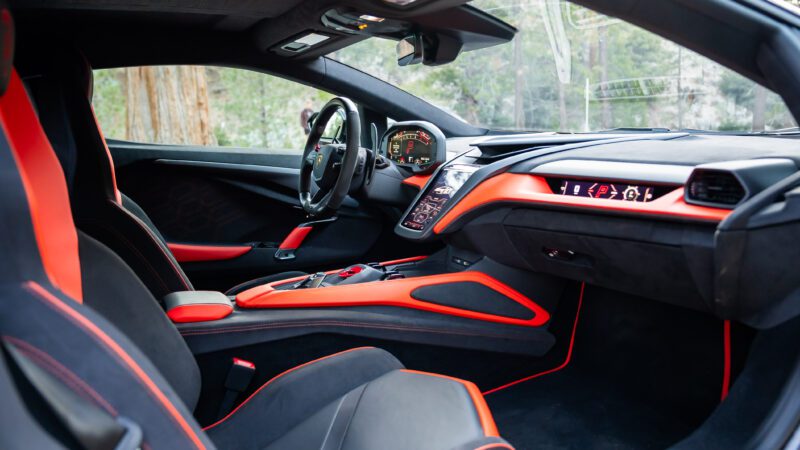 Interior of a sports car with black and orange accents, featuring a digital dashboard, steering wheel, and center console.