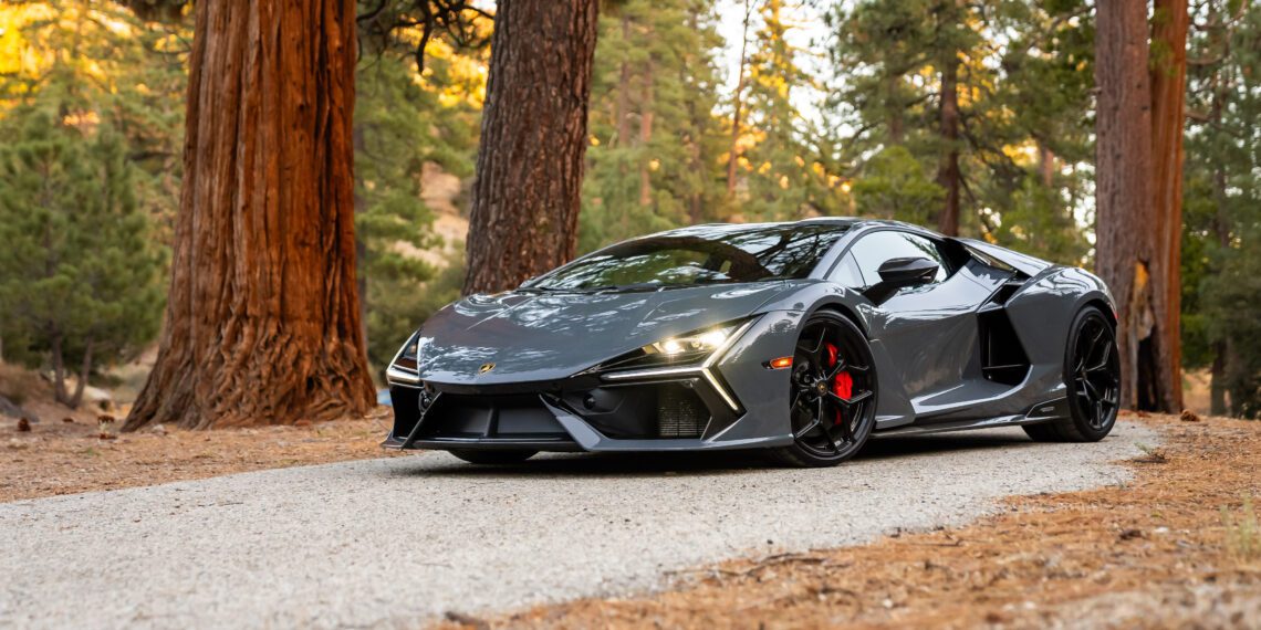 A sleek, gray sports car parked on a tree-lined road in a forest setting.