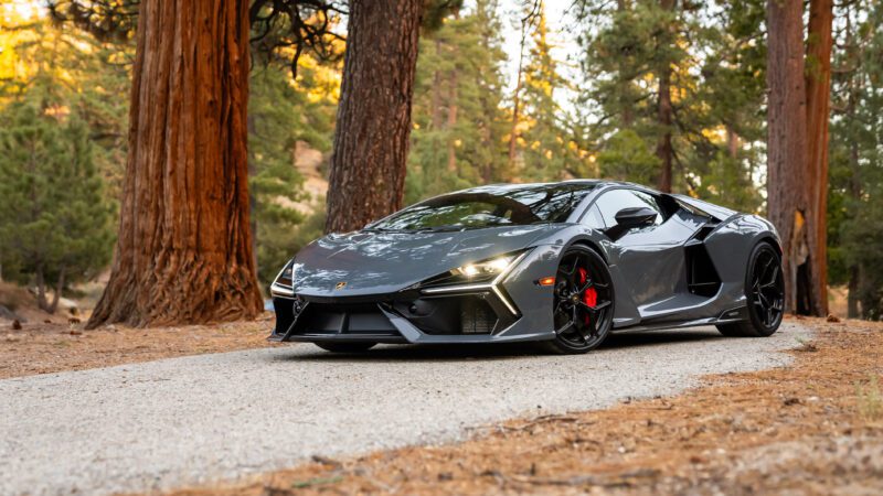 A sleek, gray sports car parked on a tree-lined road in a forest setting.