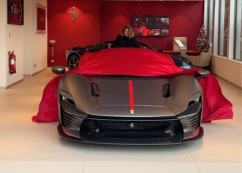 A person unveils a sleek, black sports car with red accents in a showroom.