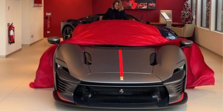 A person unveils a sleek, black sports car with red accents in a showroom.