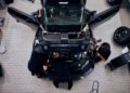 Top-down view of three mechanics working on a sleek black car reminiscent of a Ford Mustang GTD, with its hood and doors open, surrounded by tools and spare tires in a workshop. The team is focused, aiming for performance that could tackle laps under 7 minutes at Nürburgring.