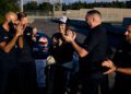 A group of men in black shirts applauds a man in a racing suit and cap standing proudly before a Ford Mustang GTD on the Nürburgring track, celebrating his impressive lap completed in under 7 minutes.