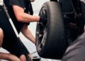 A man is kneeling and using a power tool to tighten bolts on a Ford Mustang GTD's rear wheel, readying it for an adrenaline-pumping lap around Nürburgring.