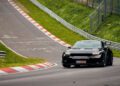 A black Ford Mustang GTD tears through the curvy, hilly racetrack of Nürburgring, surrounded by lush greenery.