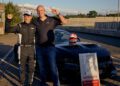 Two people stand smiling and gesturing "number one" beside a Ford Mustang GTD, with a racing helmet on the hood and a Nürburgring sign proudly displaying a lap time under 7 minutes at 6:35.