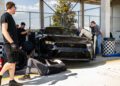 A team of people works on a sleek Ford Mustang GTD in the pit stop area, with one person underneath and others changing a tire. Their precision mirrors the focus needed to conquer the Nürburgring's legendary 7-minute lap challenge.