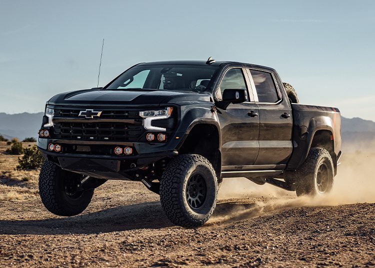 A black pickup truck from the 2024 Holiday Gift Guide powers down a dusty road in the desert landscape, echoing adventure and style—perfect for those featured in duPont REGISTRY's luxury lineup.