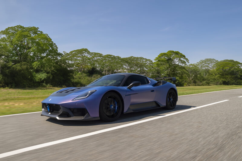 Blue sports car driving on a open road with trees in the background under a clear sky.