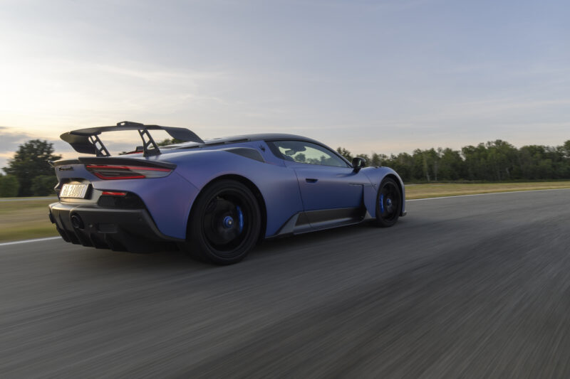 A blue sports car with a rear spoiler is driving on a track at sunset.