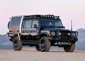 The INEOS Grenadier Quartermaster is a rugged black off-road vehicle with a custom build, featuring large tires and additional lighting, parked on a dirt terrain.