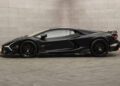 Matte black sports car with aerodynamic design and low profile, parked indoors against a gray textured wall, exuding the bespoke elegance of a custom Lamborghini by Mansory.