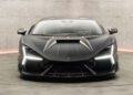 Front view of a sleek, black Mansory sports car in a modern, well-lit showroom with concrete walls.