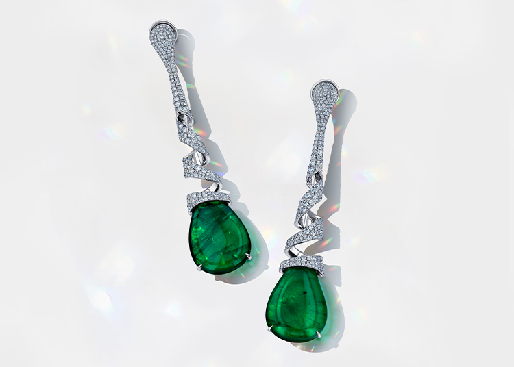 Two elegant drop earrings, highlighted in the 2024 Holiday Gift Guide, feature large green gemstones set in a twisted silver design adorned with small diamonds, displayed on a light gray background. Perfect for those looking to shop for unique and luxurious gifts.